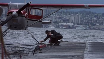 Movie still from “Trapped” (2002), directed by Luis Mandoki – A man in a black suit is fixing a plane on a pier; Wide shot, High angle