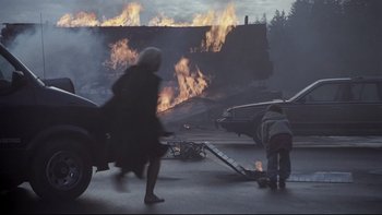 Movie still from “Trapped” (2002), directed by Luis Mandoki – A woman walking on a street near a burning building; Wide shot, High angle