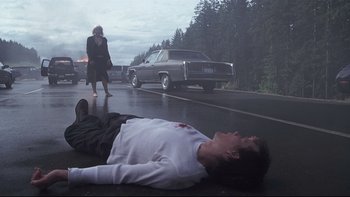 Movie still from “Trapped” (2002), directed by Luis Mandoki – A man is lying on the ground in front of a car; Wide shot, Low angle