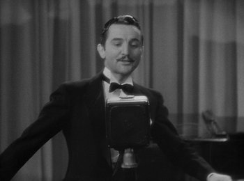 Movie still from “Trouble in Paradise” (1932), directed by Ernst Lubitsch – A black and white photo of a man singing; Close Up shot, High angle