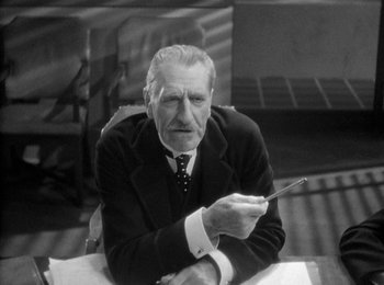 Movie still from “Trouble in Paradise” (1932), directed by Ernst Lubitsch – An older man sitting at a table holding a pencil; Medium shot, High angle