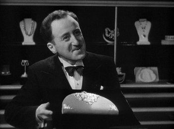 Movie still from “Trouble in Paradise” (1932), directed by Ernst Lubitsch – A man in a suit and bow tie holding a hat; Close Up shot, High angle
