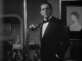 Movie still from “Trouble in Paradise” (1932), directed by Ernst Lubitsch – A man in a tuxedo standing next to a mirror in a room; Medium shot, Over the shoulder angle