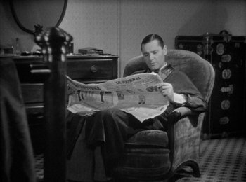 Movie still from “Trouble in Paradise” (1932), directed by Ernst Lubitsch – A black and white photo of a man sitting in a chair reading a newspaper; Medium shot, High angle
