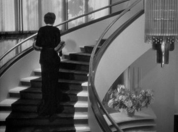 Movie still from “Trouble in Paradise” (1932), directed by Ernst Lubitsch – A woman in a black dress walking down a set of stairs; Wide shot, Low angle