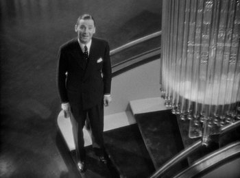 Movie still from “Trouble in Paradise” (1932), directed by Ernst Lubitsch – A black and white photo of a man in a suit standing on the stairs; Medium shot, Low angle