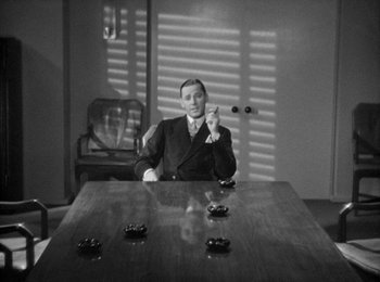 Movie still from “Trouble in Paradise” (1932), directed by Ernst Lubitsch – A man sitting at a wooden table in front of a window; Medium shot, High angle