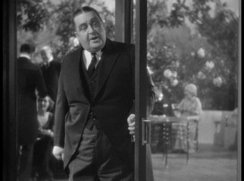 Movie still from “Trouble in Paradise” (1932), directed by Ernst Lubitsch – A man in a suit and tie standing next to a door; Medium shot, Over the shoulder angle