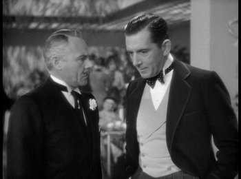 Movie still from “Trouble in Paradise” (1932), directed by Ernst Lubitsch – Two men in tuxedos talking to each other in front of a crowd; Medium shot, Over the shoulder angle
