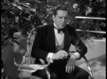 Movie still from “Trouble in Paradise” (1932), directed by Ernst Lubitsch – A black and white photo of a man sitting in a chair; Medium shot, High angle
