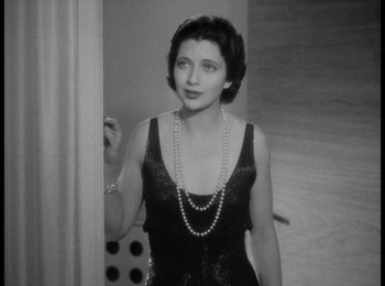 Movie still from “Trouble in Paradise” (1932), directed by Ernst Lubitsch – An old photo of a woman in a black dress and pearls; Medium shot, High angle