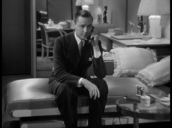 Movie still from “Trouble in Paradise” (1932), directed by Ernst Lubitsch – A black and white photo of a man sitting on a couch talking on a phone; Medium shot, High angle