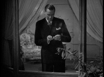 Movie still from “Trouble in Paradise” (1932), directed by Ernst Lubitsch – A black and white photo of a man in a suit looking at his cell phone; Medium shot, Low angle