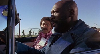 Movie still from “Truck Turner” (1974), directed by Jonathan Kaplan – Two men are driving in a car on a sunny day; Medium shot, Low angle