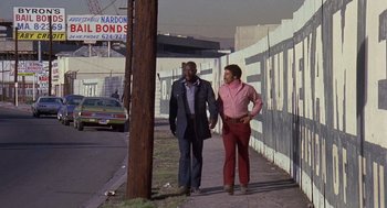 Movie still from “Truck Turner” (1974), directed by Jonathan Kaplan – Two men walking down the street holding hands; Wide shot, Low angle