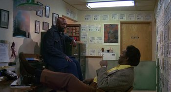 Movie still from “Truck Turner” (1974), directed by Jonathan Kaplan – Two men are sitting in a room talking to each other; Wide shot, High angle