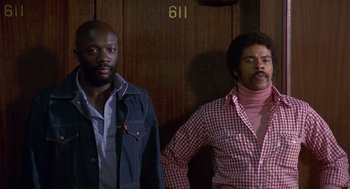 Movie still from “Truck Turner” (1974), directed by Jonathan Kaplan – A couple of men standing next to each other in a room; Medium shot, Low angle