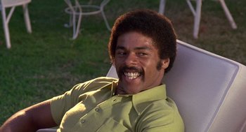 Movie still from “Truck Turner” (1974), directed by Jonathan Kaplan – A man sitting in a lawn chair smiling for the camera; Close Up shot, Low angle