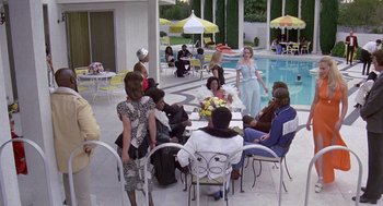 Movie still from “Truck Turner” (1974), directed by Jonathan Kaplan – A group of people sitting around a table near a swimming pool; Wide shot, High angle