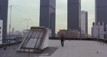 Movie still from “Truck Turner” (1974), directed by Jonathan Kaplan – A man walking across a roof top in front of two skyscrapers; Wide shot, Low angle