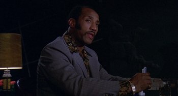 Movie still from “Truck Turner” (1974), directed by Jonathan Kaplan – A man wearing a suit and tie sitting in front of a microphone; Close Up shot, Low angle