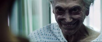 Movie still from “Truth or Dare” (2018), directed by Jeff Wadlow – An old woman with a very big smile on her face; Extreme Close Up shot, Over the shoulder angle