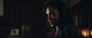 Movie still from “Truth or Dare” (2018), directed by Jeff Wadlow – A young woman smiles for the camera in a dark room; Close Up shot, Over the shoulder angle