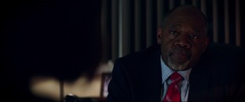 Movie still from “Truth or Dare” (2018), directed by Jeff Wadlow – A man wearing a suit and tie sitting in front of a window; Close Up shot, Over the shoulder angle