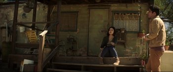 Movie still from “Truth or Dare” (2018), directed by Jeff Wadlow – A woman sitting on a wooden platform in front of a house; Wide shot, Low angle