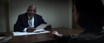 Movie still from “Truth or Dare” (2018), directed by Jeff Wadlow – A man sitting at a table in front of another man holding papers; Medium shot, Over the shoulder angle