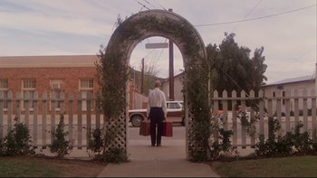 Movie still from “Twilight Zone: The Movie” (1983), directed by Steven Spielberg – A man holding two red suitcases in front of an archway; Wide shot, Low angle