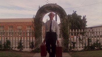 Movie still from “Twilight Zone: The Movie” (1983), directed by Steven Spielberg – An older man holding two suitcases in front of an archway; Wide shot, Low angle