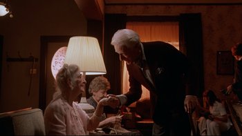 Movie still from “Twilight Zone: The Movie” (1983), directed by Steven Spielberg – An older man in a suit is feeding a woman a piece of cake; Medium shot, Over the shoulder angle
