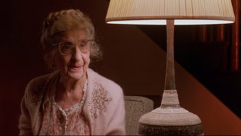 Movie still from “Twilight Zone: The Movie” (1983), directed by Steven Spielberg – An older woman sitting in front of a table lamp; Close Up shot, Over the shoulder angle