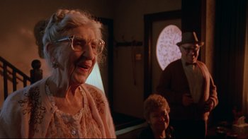 Movie still from “Twilight Zone: The Movie” (1983), directed by Steven Spielberg – An older woman wearing glasses is smiling at the camera; Medium shot, Over the shoulder angle