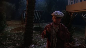 Movie still from “Twilight Zone: The Movie” (1983), directed by Steven Spielberg – A man in a hat and a coat standing in a yard; Medium shot, High angle