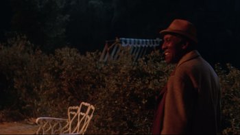Movie still from “Twilight Zone: The Movie” (1983), directed by Steven Spielberg – A man wearing a hat standing next to a table; Medium shot, Over the shoulder angle