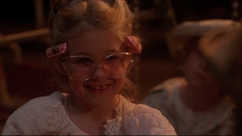 Movie still from “Twilight Zone: The Movie” (1983), directed by Steven Spielberg – A little girl wearing glasses and smiling for the camera; Close Up shot, Over the shoulder angle