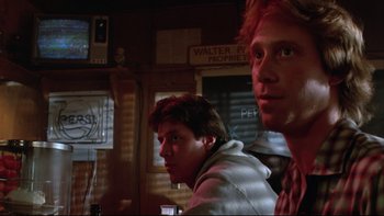 Movie still from “Twilight Zone: The Movie” (1983), directed by Steven Spielberg – Two young men are sitting in front of a sign; Close Up shot, Low angle