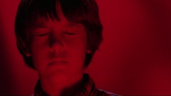Movie still from “Twilight Zone: The Movie” (1983), directed by Steven Spielberg – A young boy with his eyes closed in a red room; Close Up shot, Low angle