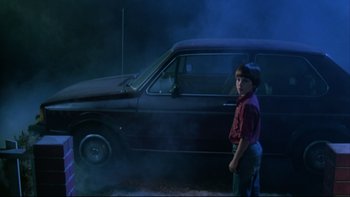 Movie still from “Twilight Zone: The Movie” (1983), directed by Steven Spielberg – A boy standing in front of a car in the dark; Wide shot, Low angle
