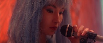 Movie still from “Twin Dragons” (1992), directed by Ringo Lam – A woman with blue hair is holding a microphone; Extreme Close Up shot, Over the shoulder angle