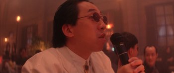 Movie still from “Twin Dragons” (1992), directed by Ringo Lam – A man in a white dress shirt and tie holding a microphone; Close Up shot, Low angle