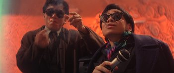 Movie still from “Twin Dragons” (1992), directed by Ringo Lam – A man smoking a cigarette while another man holds a cigarette holder; Medium shot, Low angle
