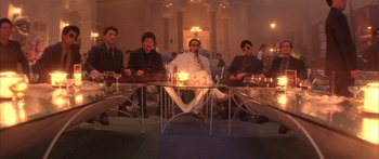 Movie still from “Twin Dragons” (1992), directed by Ringo Lam – A group of men sitting around a glass table; Wide shot, Low angle