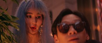 Movie still from “Twin Dragons” (1992), directed by Ringo Lam – A man and a woman wearing sunglasses posing for a picture; Close Up shot, Over the shoulder angle