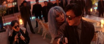 Movie still from “Twin Dragons” (1992), directed by Ringo Lam – A woman with blue hair is holding a gun while standing next to a man with blue hair; Close Up shot, Over the shoulder angle