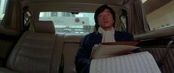 Movie still from “Twin Dragons” (1992), directed by Ringo Lam – A man sitting in the back seat of a car holding papers; Medium shot, High angle