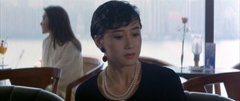 Movie still from “Twin Dragons” (1992), directed by Ringo Lam – A woman with short black hair wearing a necklace; Close Up shot, Over the shoulder angle