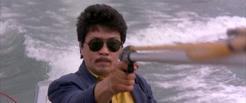 Movie still from “Twin Dragons” (1992), directed by Ringo Lam – A man in a yellow shirt is holding a gun; Close Up shot, Low angle